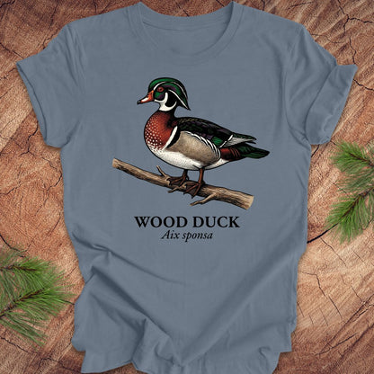 Blue t-shirt with a wood duck graphic and text on a wooden surface.