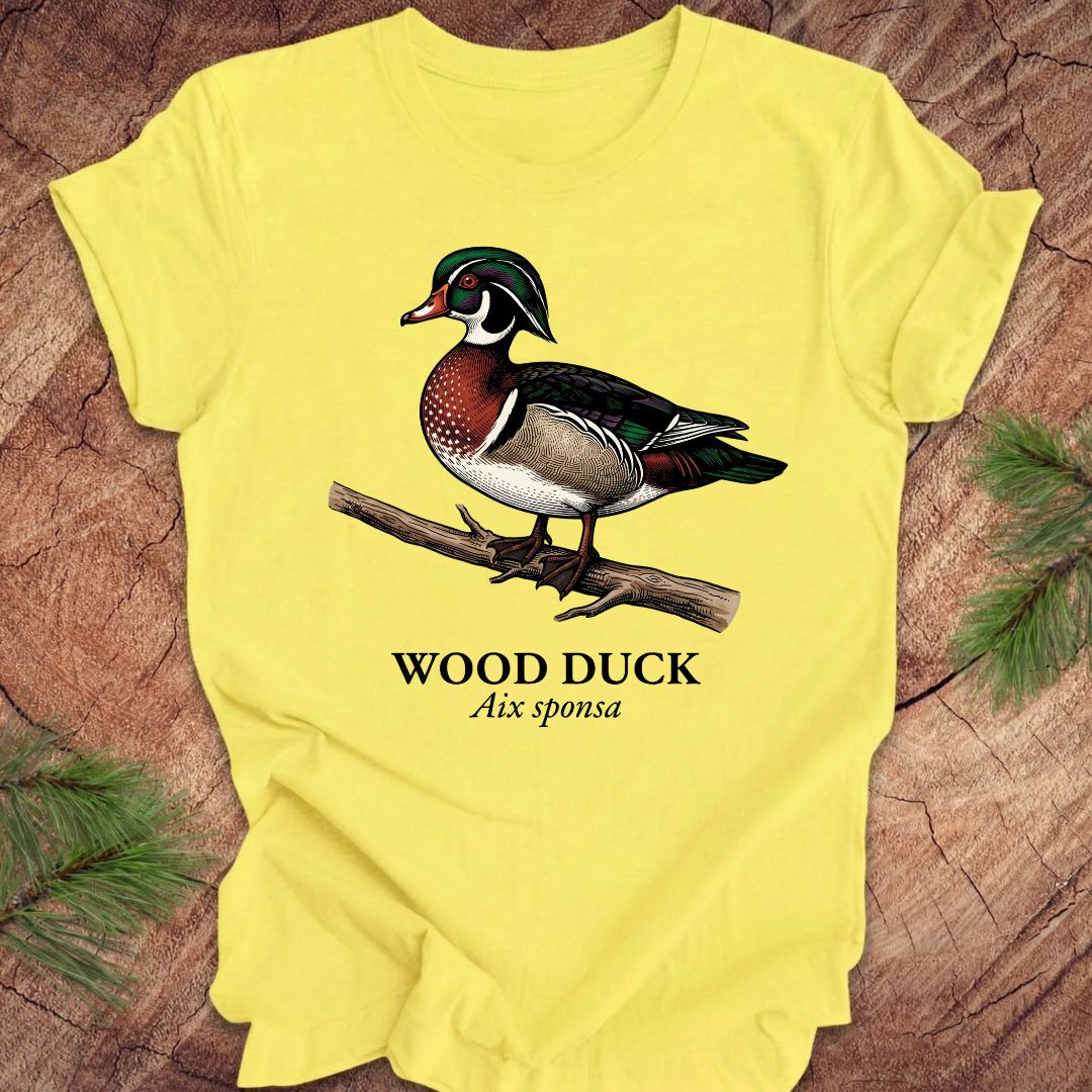 Yellow t-shirt with a wood duck graphic and text on a wooden surface.