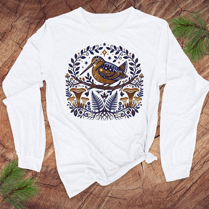 White long-sleeve shirt with woodcock nature-themed design on a wooden surface