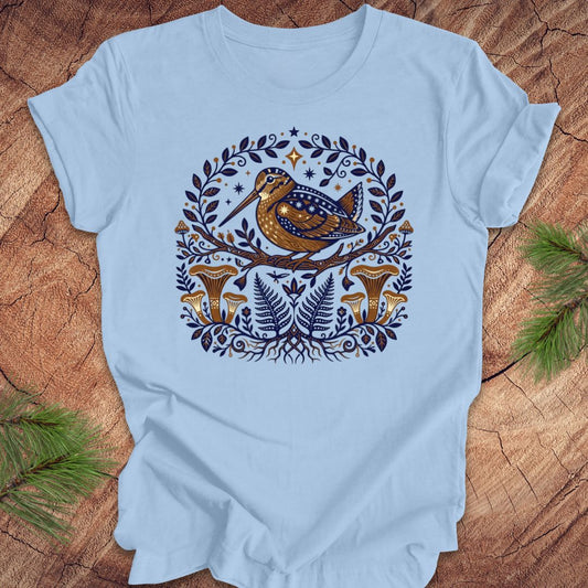 Light blue t-shirt with a woodcock and mushroom design on a wooden surface