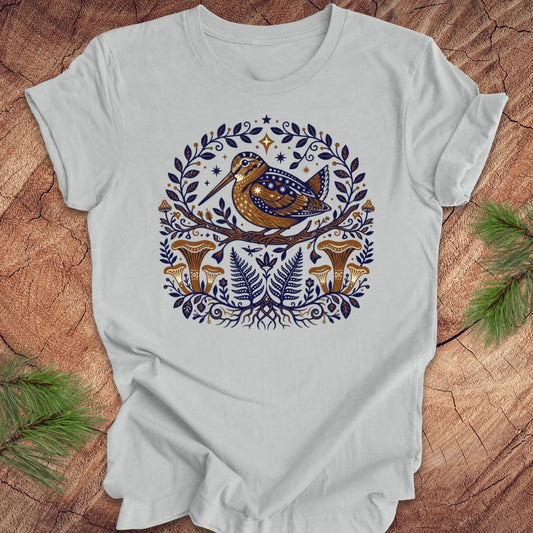 Silver t-shirt with a woodcock and mushroom design on a wooden surface