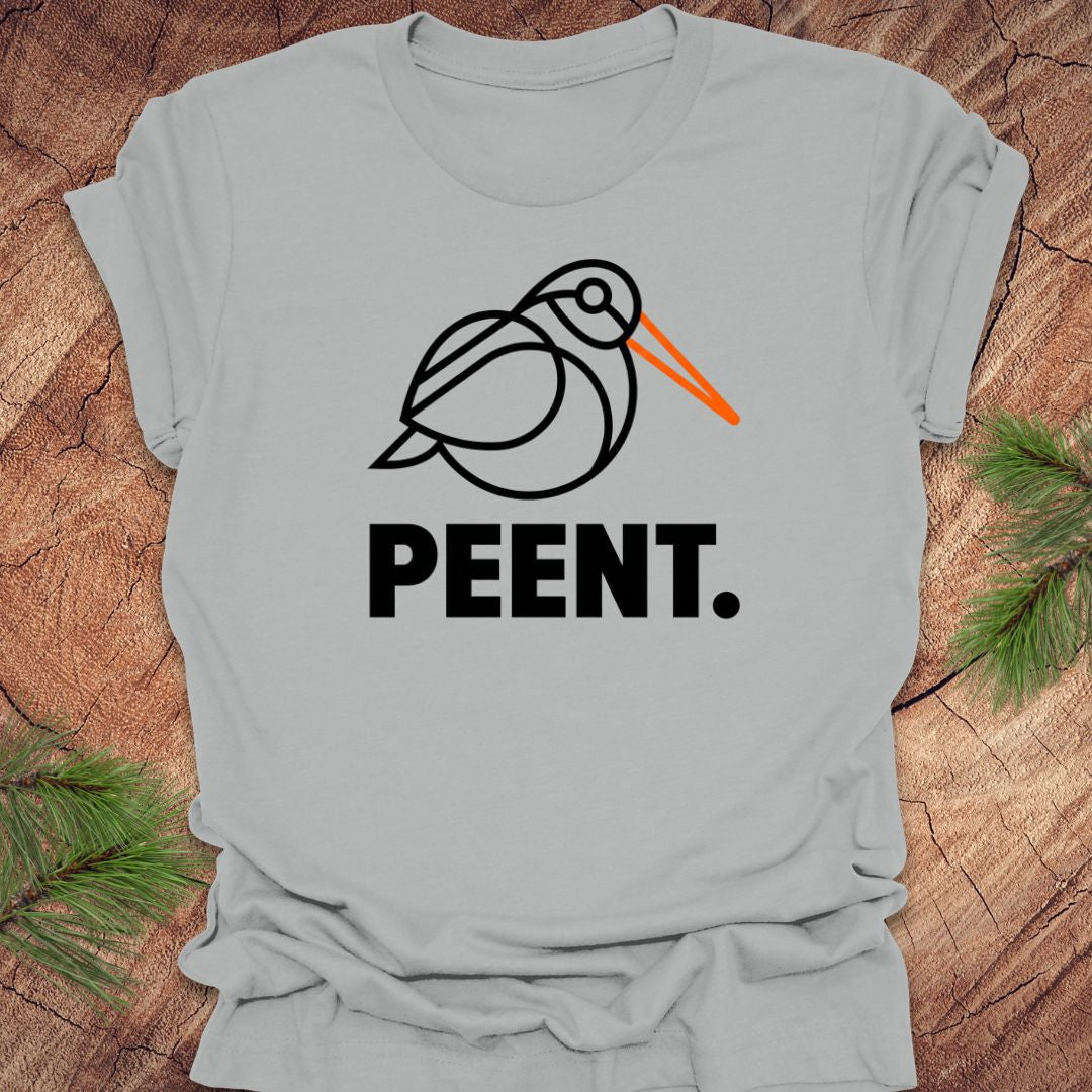 Silver t-shirt with a woodcock graphic and 'PEENT.' text on a wooden surface.