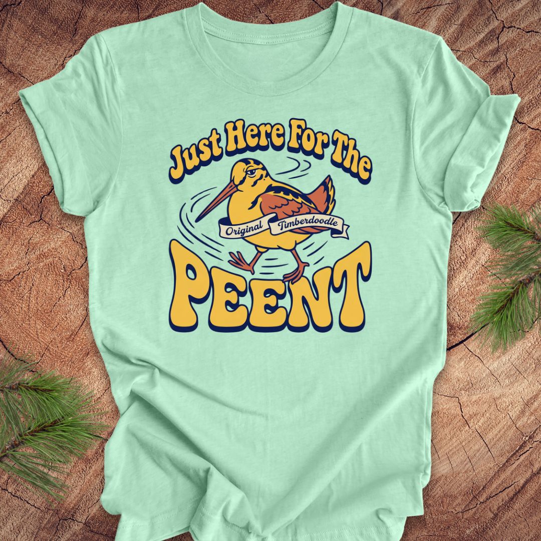 Mint green t-shirt with 'Just Here For The Peent' woodcock graphic on a wooden surface