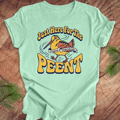 Mint green t-shirt with 'Just Here For The Peent' woodcock graphic on a wooden surface
