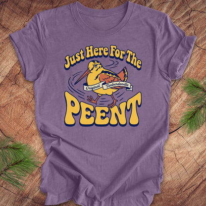 Purple t-shirt with 'Just Here For The Peent' woodcock graphic on a wooden surface