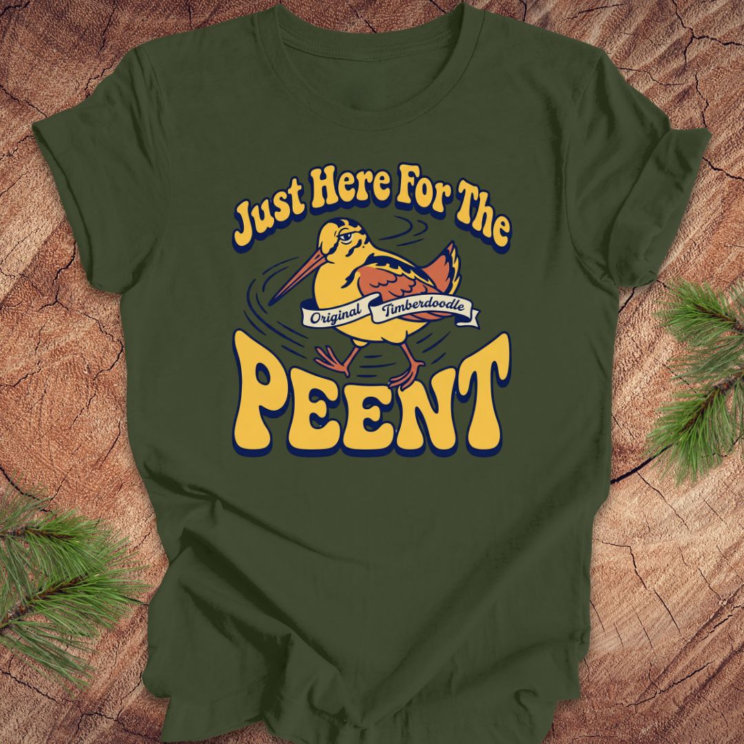 Green t-shirt with 'Just Here For The Peent' woodcock graphic on a wooden surface