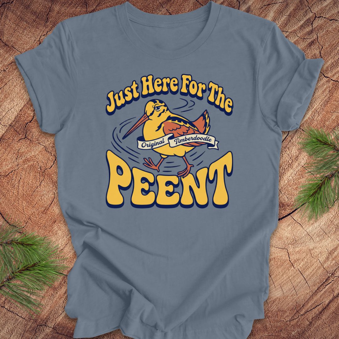 Blue t-shirt with 'Just Here For The Peent' woodcock graphic on a wooden surface