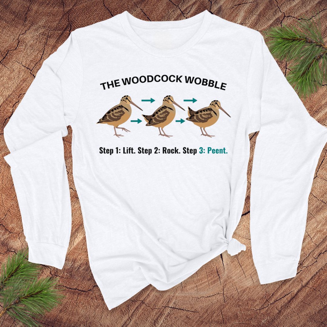 White long-sleeve shirt with woodcock wobble graphic on a wooden surface