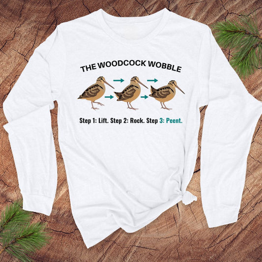 White long-sleeve shirt with woodcock wobble graphic on a wooden surface