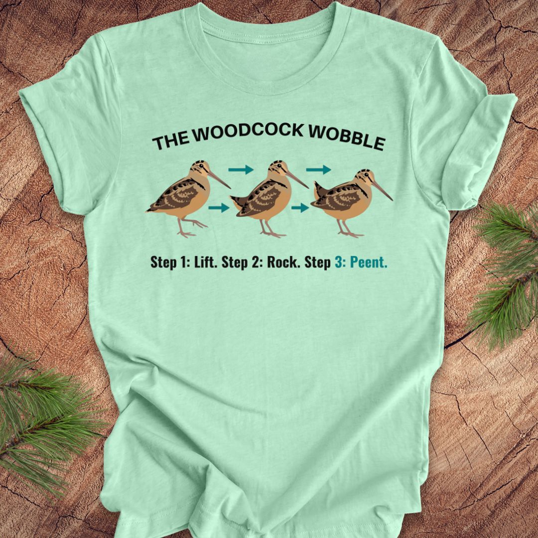 Light green t-shirt with woodcock wobble graphic and text on a wooden surface