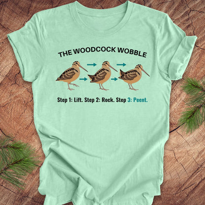 Light green t-shirt with woodcock wobble graphic and text on a wooden surface