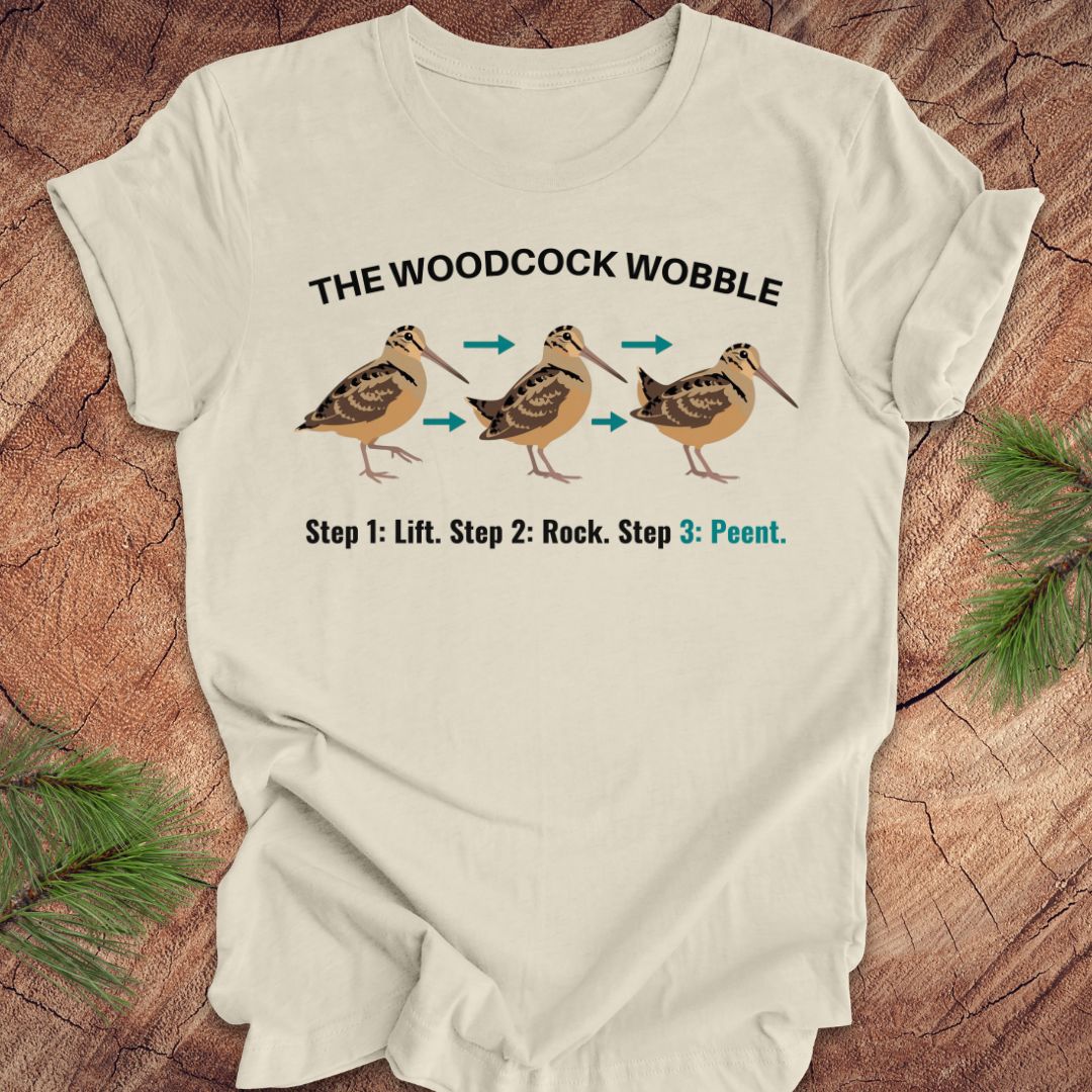 Beige t-shirt with woodcock wobble graphic and text on a wooden surface