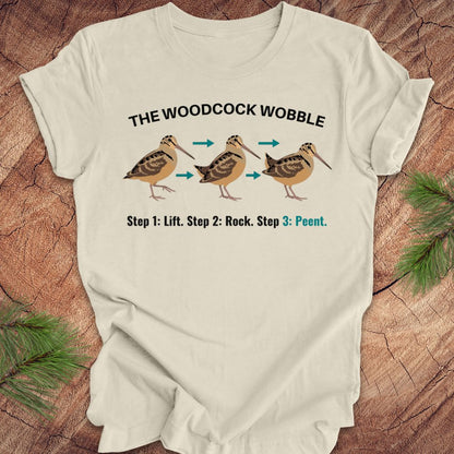 Beige t-shirt with woodcock wobble graphic and text on a wooden surface