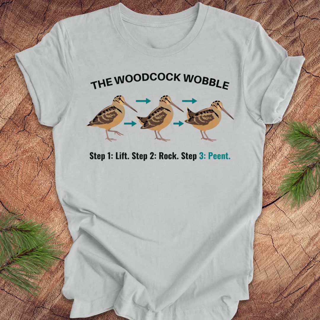 Silver t-shirt with woodcock wobble graphic and text on a wooden surface