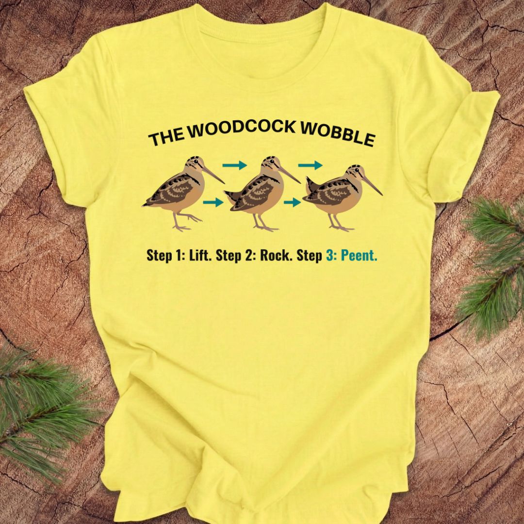 Yellow t-shirt with 'The Woodcock Wobble' graphic and text on a wooden surface.