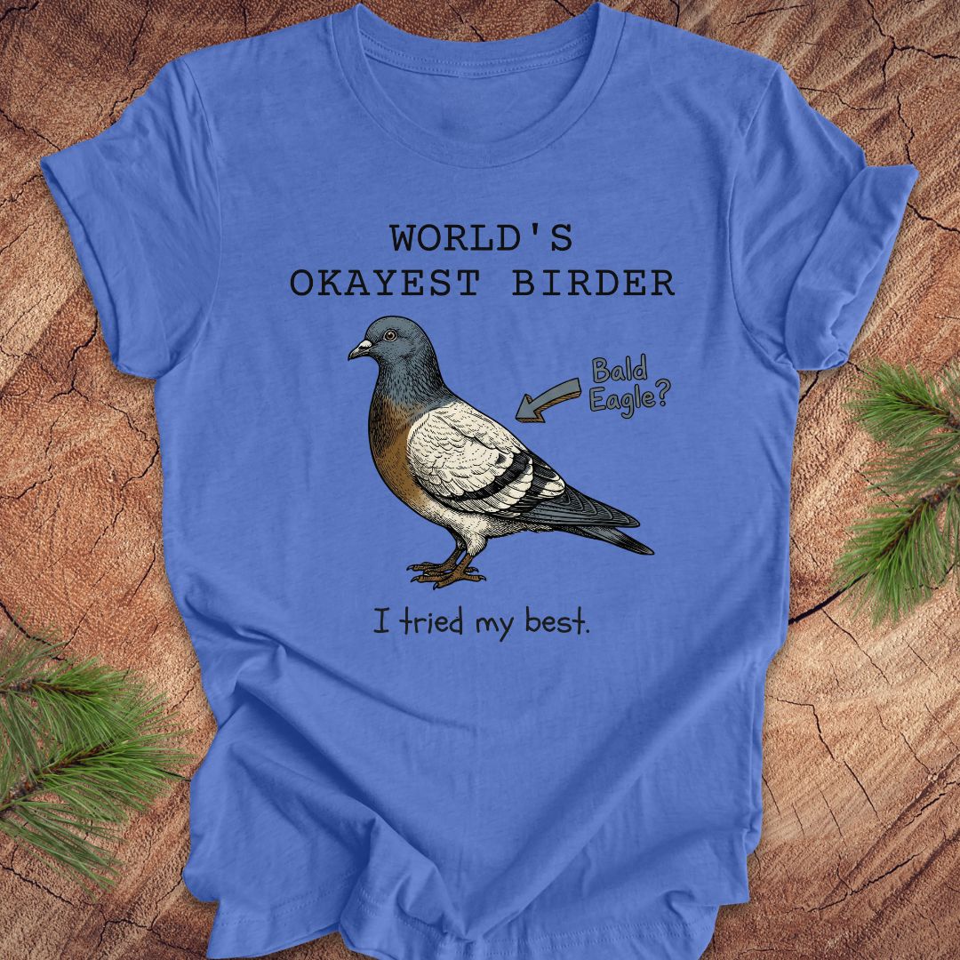 Blue t-shirt with a pigeon illustration and text, 'world's okayest birder' on a wooden surface