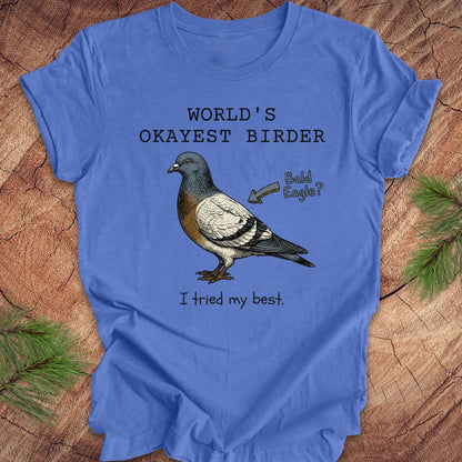 Blue t-shirt with a pigeon illustration and text, 'world's okayest birder' on a wooden surface