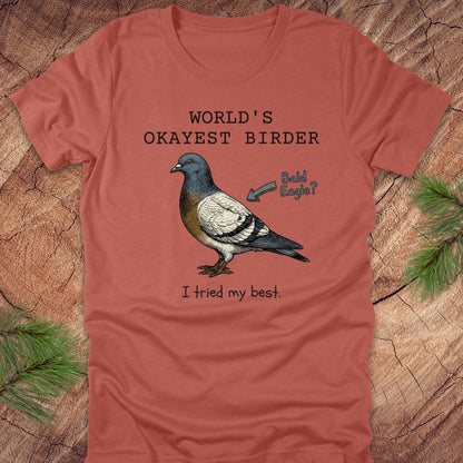 Clay colored t-shirt with a pigeon graphic and text, "world's okayest birder' on a wooden surface