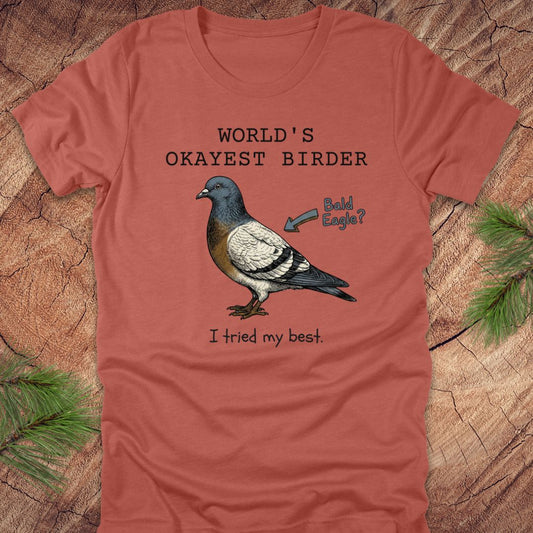 Clay colored t-shirt with a pigeon graphic and text, "world's okayest birder' on a wooden surface