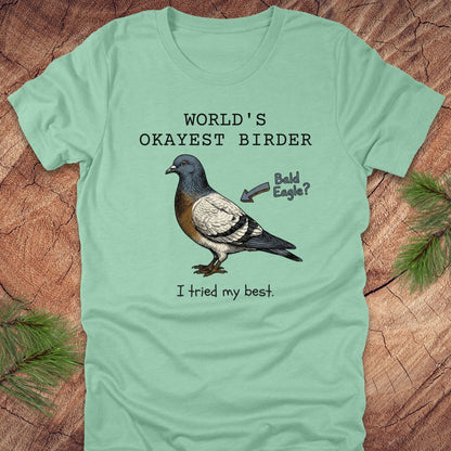 Mint green t-shirt with a pigeon graphic and text, "world's okayest birder' on a wooden surface