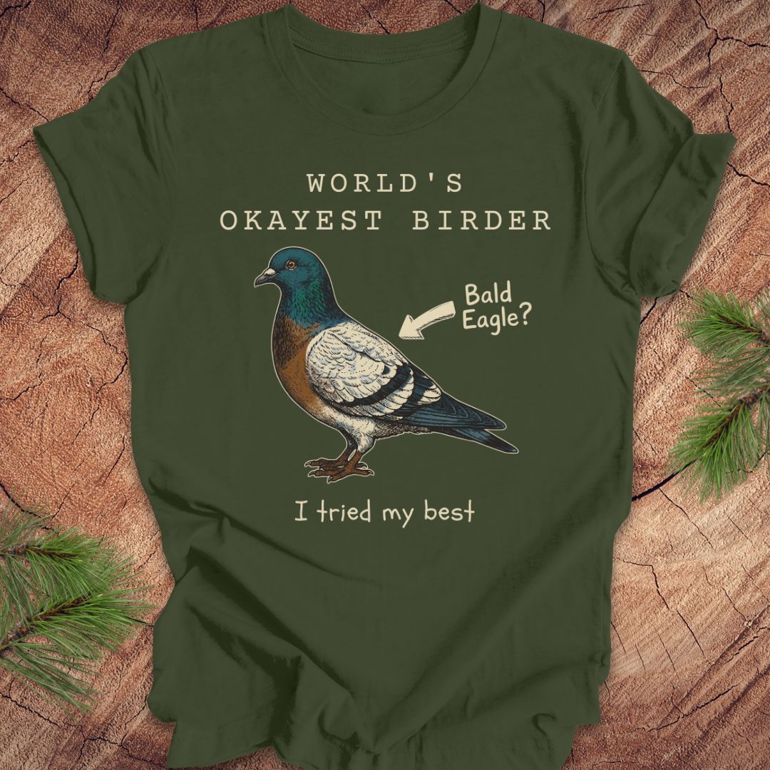 Green t-shirt with a pigeon graphic and text, 'world's okayest birder' on a wooden surface