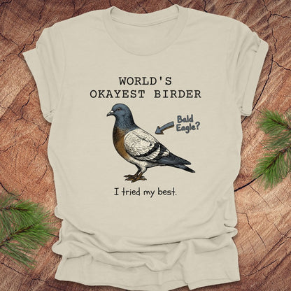 Beige t-shirt with a pigeon graphic and text, "world's okayest birder' on a wooden surface