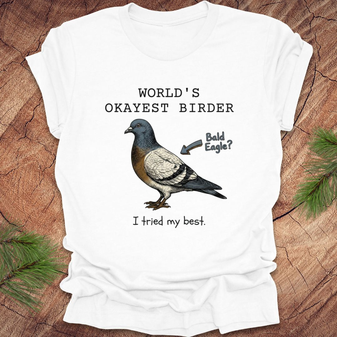 White t-shirt with a pigeon graphic and text, "world's okayest birder' on a wooden surface
