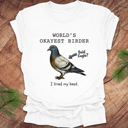 White t-shirt with a pigeon graphic and text, "world's okayest birder' on a wooden surface