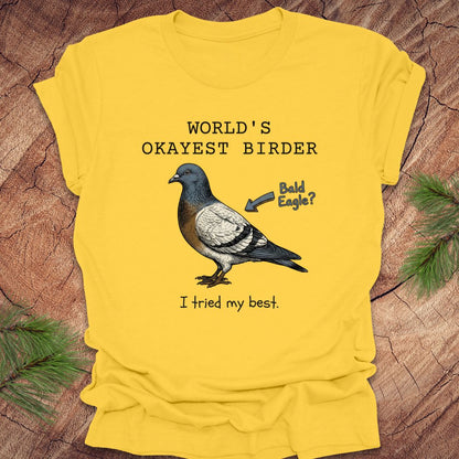 Yellow t-shirt with a pigeon graphic and text, "world's okayest birder' on a wooden surface