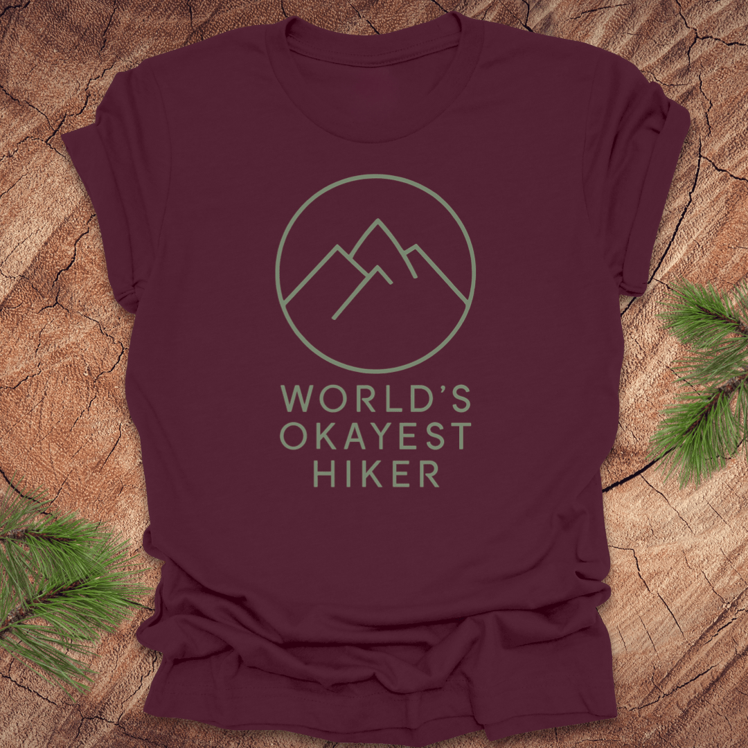 Maroon t-shirt with mountain graphic and 'World's Okayest Hiker' text on a wooden surface.