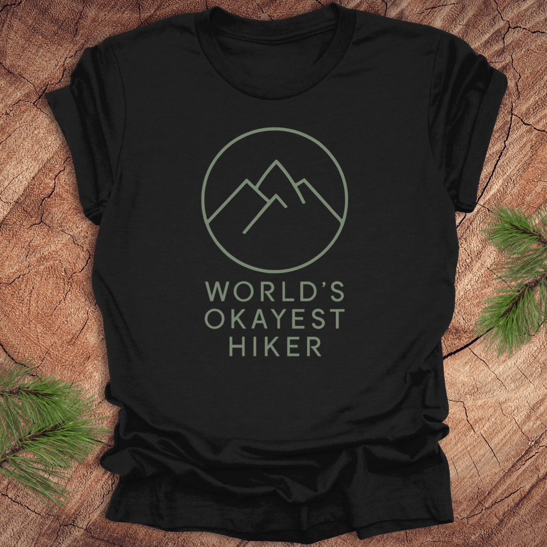 Black t-shirt with 'World's Okayest Hiker' text and mountain graphic on a wooden surface.