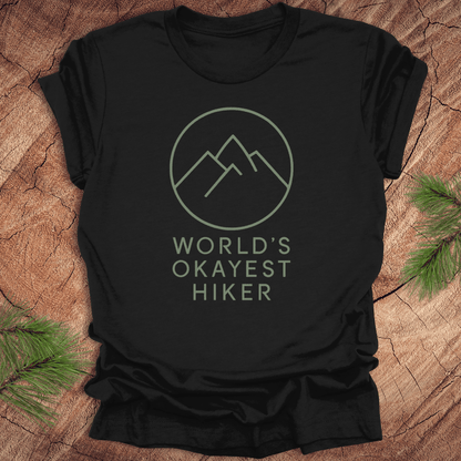 Black t-shirt with 'World's Okayest Hiker' text and mountain graphic on a wooden surface.