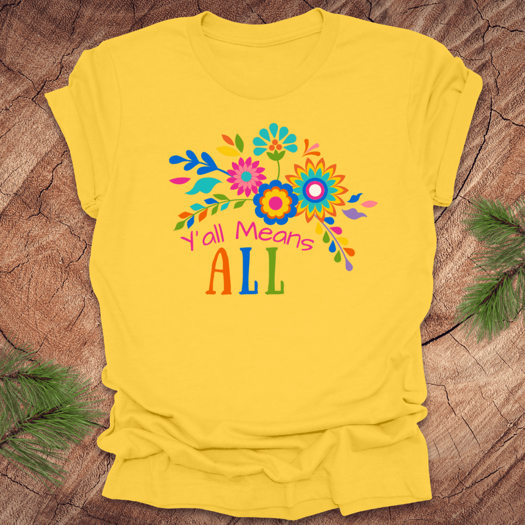 Yellow t-shirt with colorful floral design and text 'Y'all Means All' on a wooden surface