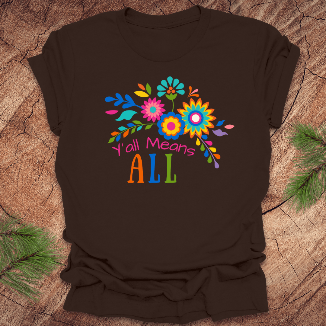 Brown t-shirt with colorful floral design and text 'Y'all Means All' on a wooden surface
