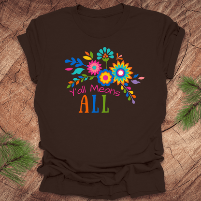 Brown t-shirt with colorful floral design and text 'Y'all Means All' on a wooden surface