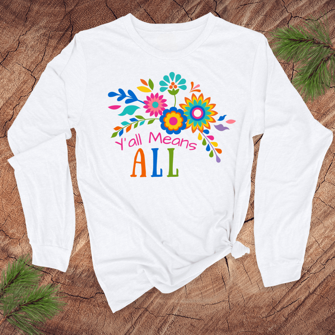 White long sleeve tshirt with colorful floral design and text, 'Y'all Means All' on a wooden surface