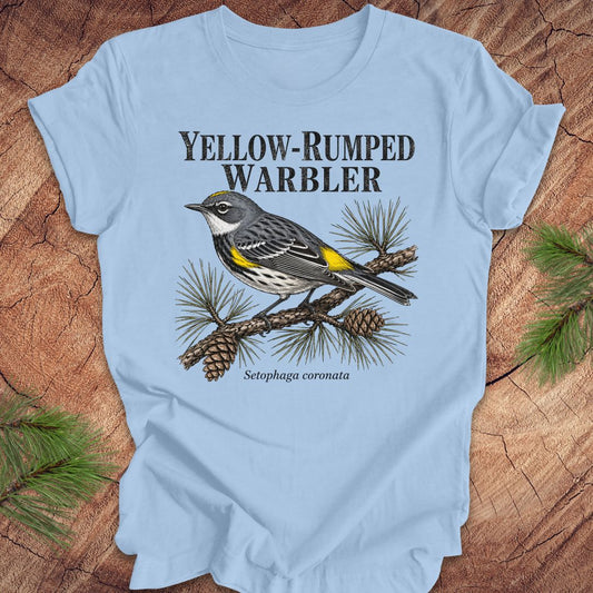 Light blue t-shirt with yellow-rumped warbler graphic and text on a wooden surface.