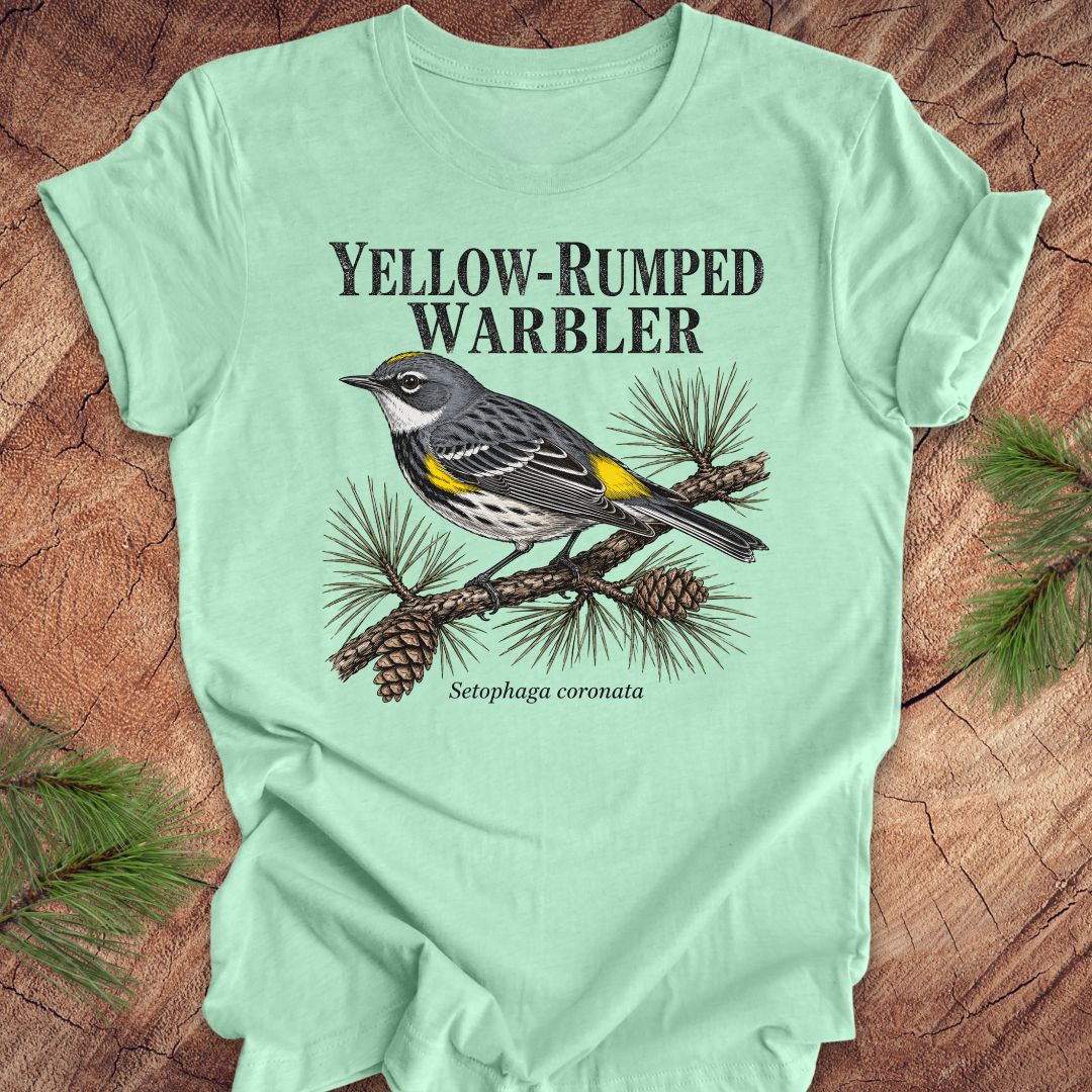 Light green t-shirt with yellow-rumped warbler graphic and text on a wooden surface.
