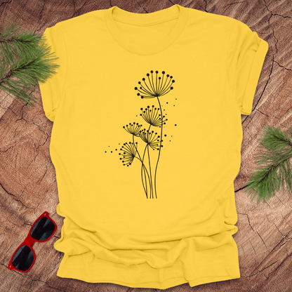 Yellow t-shirt with black floral dandelion design on a wooden surface with sunglasses and greenery.