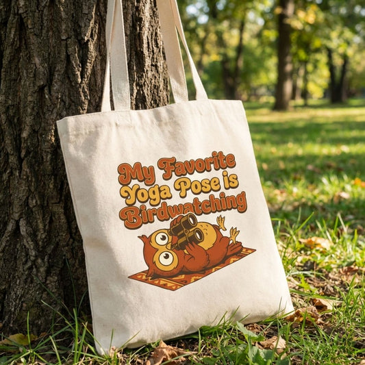 Tote bag with owl design and text 'My Favorite Yoga Pose is Birdwatching' leaning against a tree in a park.