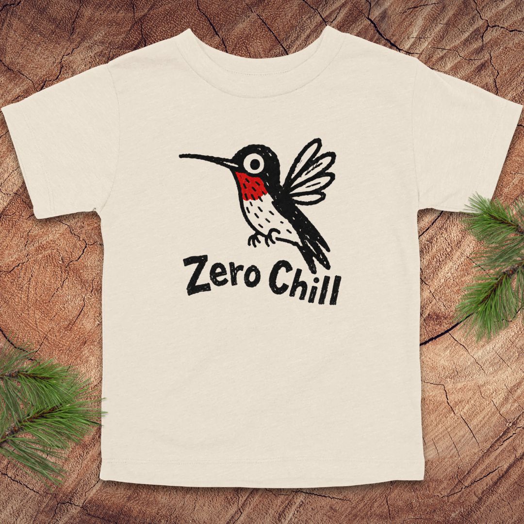 Beige t-shirt with a black and white bird graphic and 'Zero Chill' text on a wooden surface.
